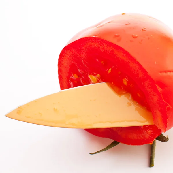 Der Rand eines roten Messers schneidet eine rote Tomate mit einem Bein auf einem weißen — Stockfoto