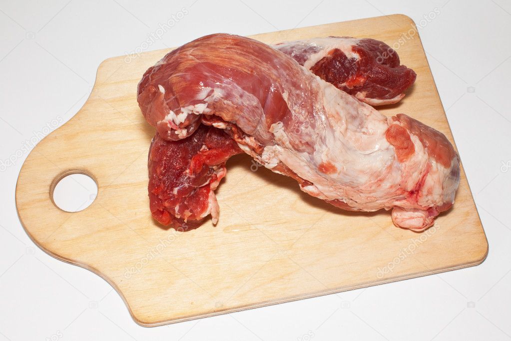 Two piece of crude meat with blood on a wooden chopping board on