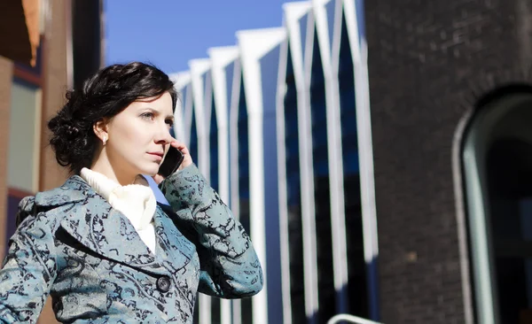 Portret van een mooi meisje met een mobiele telefoon op de achtergrond van een zakelijke gebouw — Stockfoto