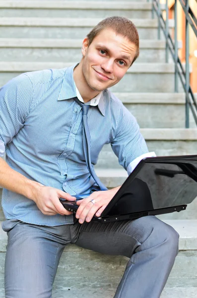 年轻的小伙子坐在楼梯上的一台笔记本电脑 — 图库照片