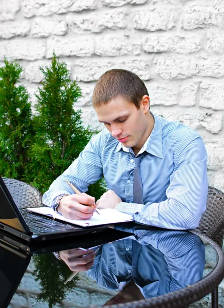 Geschäftsmann mit Laptop im Café auf der Straße. macht Notizen mit Stift — Stockfoto
