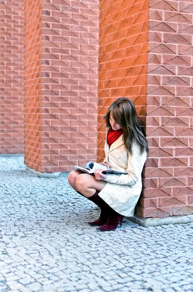 Vrouwelijke zit en leest een boek bij de muur — Stockfoto