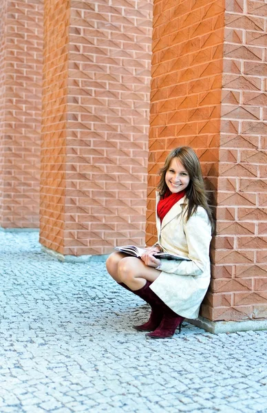 Lachende vrouw zit en leest een boek bij de muur — Stockfoto