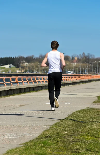 Hombre joven atlético corriendo en la costa. Desde atrás. — Foto de Stock
