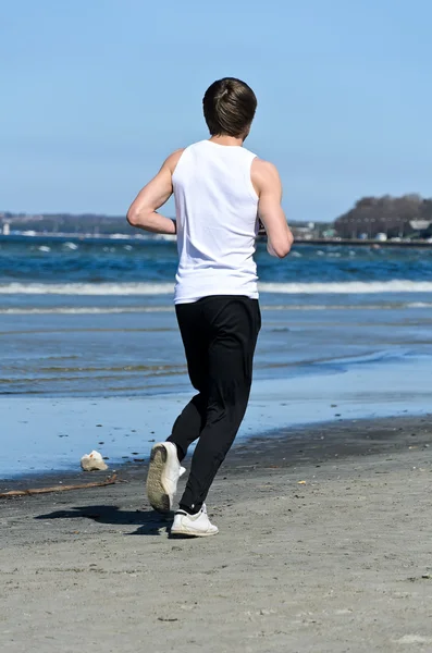 Homem jovem atlético correndo na praia. Na parte de trás — Fotografia de Stock