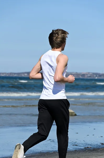 Homem jovem atlético correndo na praia. Na parte de trás . — Fotografia de Stock