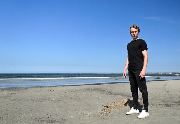Молодой мужчина в черной одежде и белых туфлях стоит на пляже — стоковое фото