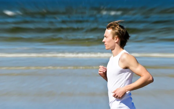 Motion blur: Athletic young male running on the beach — Stock Photo, Image