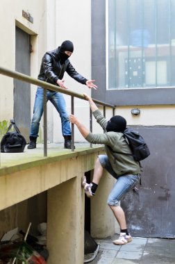 Escape from a robbery. One tries to help another to climb the rails. clipart