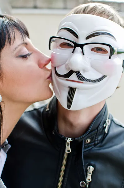 Kvinna kysser man i vendetta mask i glas. — Stockfoto