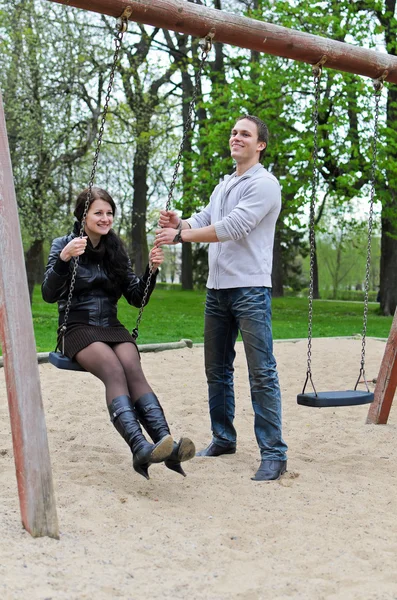 Guy rohlíky dívku na houpačce v parku. — Stock fotografie