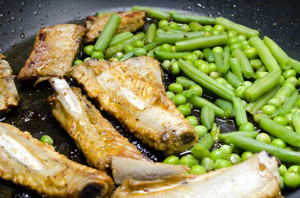 Pork ribs with peas and green beans prepared in a frying pan — Stock Photo, Image