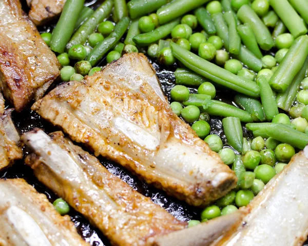 Pork ribs with peas and green beans prepared in a frying pan — Stock Photo, Image