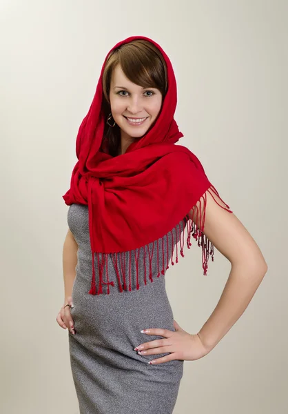 Unga leende kvinna i en röd halsduk. på grå bakgrund. — Stockfoto