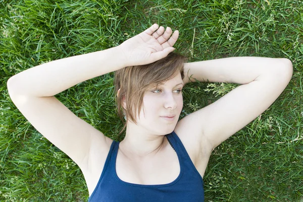 Aantrekkelijk meisje in blauw shirt is rusten op het gras. — Stockfoto