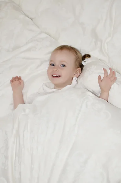 Забавная маленькая девочка лежит на кровати под одеялом . — стоковое фото