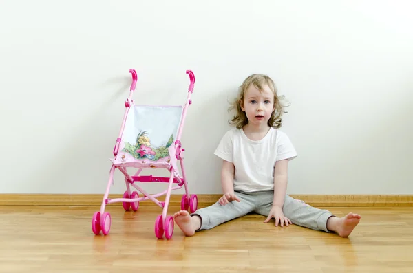 小可爱的女孩坐在玩具婴儿车旁边的地板上 — 图库照片