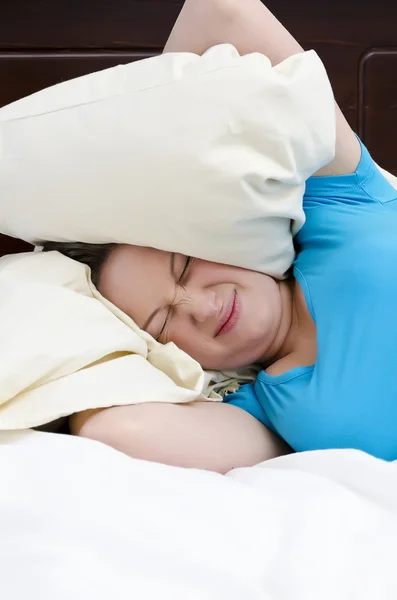 Young woman covering ears with pillow because of noise. — Stock Photo, Image
