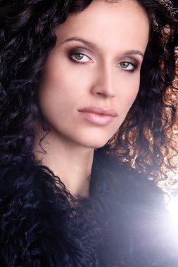 Portrait of a young Brazilian fashion glamour model and green eyes wearing fur playing with dark brown curly hair clipart