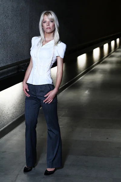 Young blonde model girl close up portrait in her early 30s or 20s looking straight in a white shirt with a white pearls with flare lights on the background in a tunnel — Stock Photo, Image