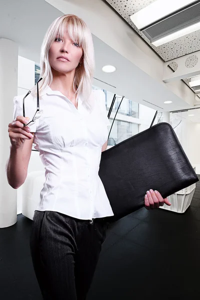 stock image Young attractive blonde business women serious wearing glasses holding a folder in an office environment walking