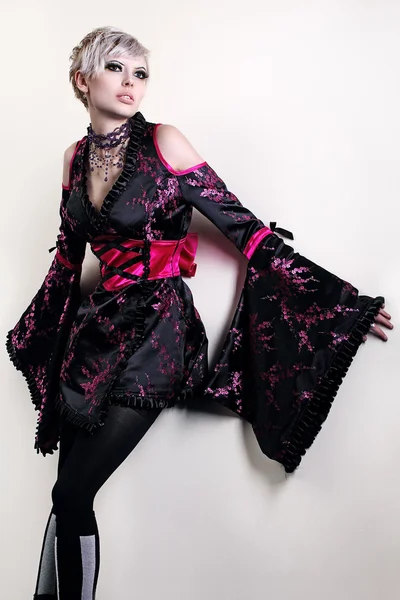 Ασυνήθιστο μόδας της νεανικής μόδας ξανθό μοντέλο, ποζάρει φορώντας ένα παράξενο μαύρο κόκκινο φόρεμα στούντιο shot μικτή αστραπή ταχύτητα κλείστρου — Φωτογραφία Αρχείου