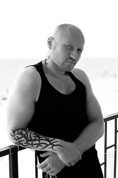 Un homme chauve sportif fort avec des tatouages sur un balcon de l'hôtel au bord de la mer Noire — Photo
