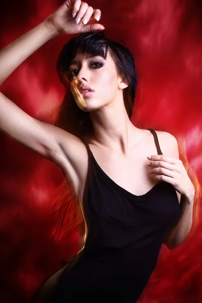 Joven morena en vestido negro posando sobre fondo rojo — Foto de Stock