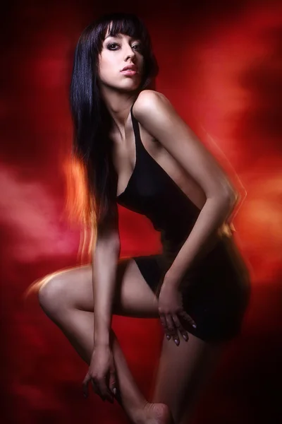 Giovane signora bruna in abito nero in posa su sfondo rosso — Foto Stock