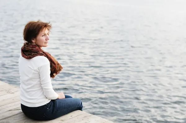 Woman sitting on wood boards by the water — Stock Photo, Image