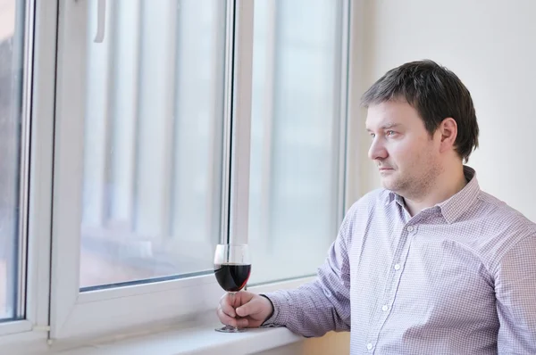 Człowiek lampkę wina, patrząc w okno — Zdjęcie stockowe