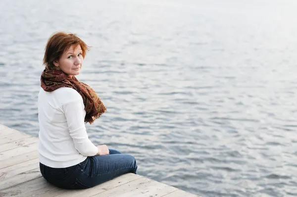 Woman sitting on wood boards by the water — Stock Photo, Image