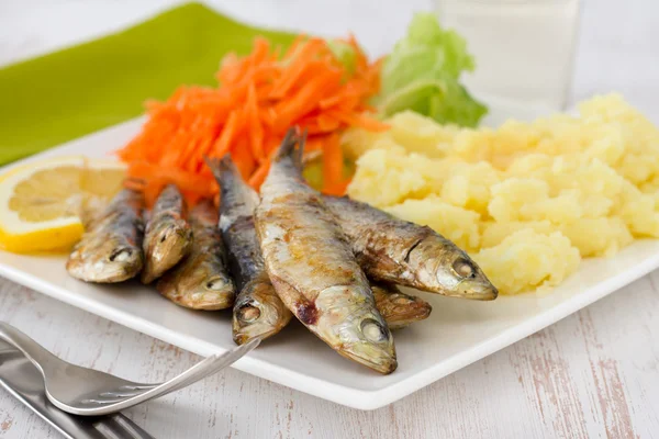 Smažené sardinky se salátem a šťouchané brambory na talíři — Stock fotografie
