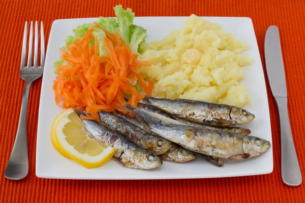 Жареные сардины с салатом и пюре на тарелке — стоковое фото