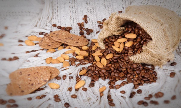 Chocolate cookies, coffee beans and almonds on canvas background — Stock Photo, Image