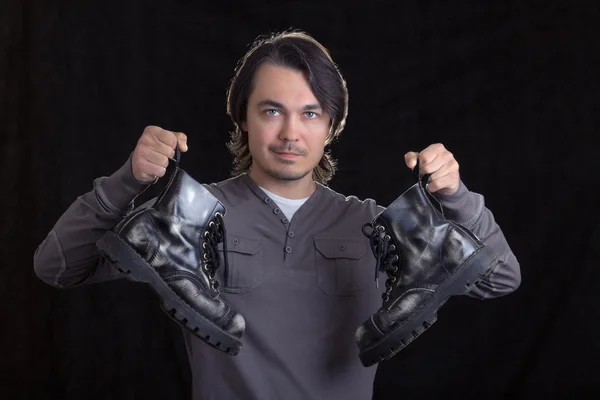 Young man holding old black boots in his hands — Stock Photo, Image