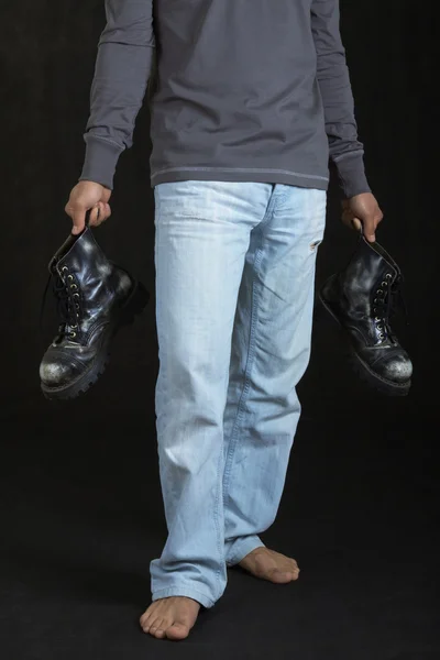 Young man holding a pair of shoes on black — Stock Photo, Image