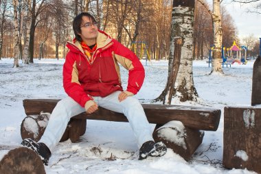 Young man sitting on bench in winter park clipart