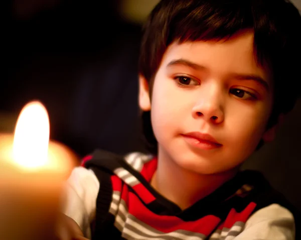 Красивый мальчик смотрит на пламя свечи ночью — стоковое фото