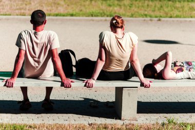 Young soaking up the sun on the bench clipart