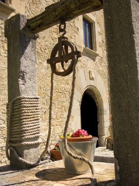Vieux puits avec des fleurs de décoration dans le seau, avec une maison de classe derrière — Photo
