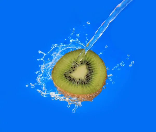 Acqua spruzzata su kiwi metà su sfondo blu — Foto Stock