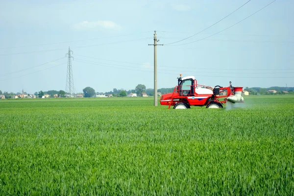 Red tractor waters a cultivated field in farmlands — Stock Photo, Image