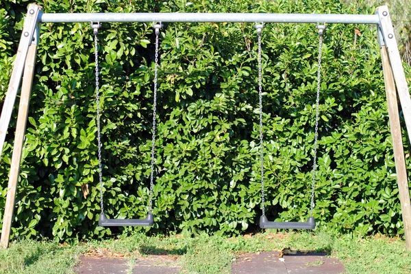 Dos columpios en el parque, con hojas verdes en el fondo —  Fotos de Stock