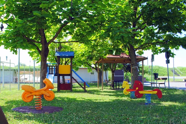 Grüner Kinderspielplatz mit Plastikspielen lizenzfreie Stockbilder