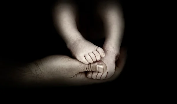 Baby's voeten in handen van de vader op de monochrome achtergrond — Stockfoto