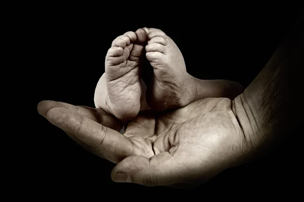 Babys Füße in den Händen des Vaters auf dem monochromen Hintergrund — Stockfoto