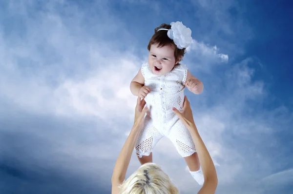 Bambino in bianco nelle mani della madre sotto lo sfondo del cielo — Foto Stock