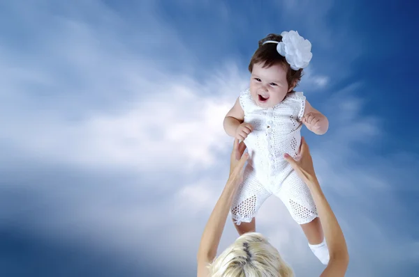 Kind in wit in moeder handen onder hemelachtergrond — Stockfoto