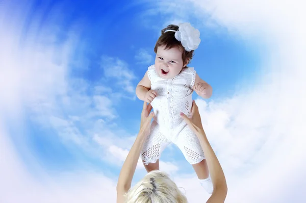 Kind in wit in moeder handen onder hemelachtergrond — Stockfoto